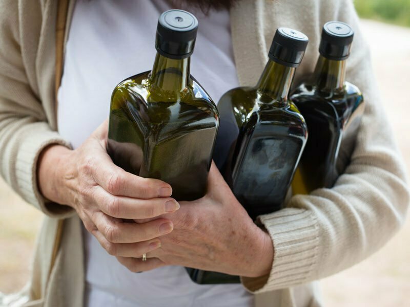 Person holding 3 dark green bottles of olive oil at CERES Olives to Oil